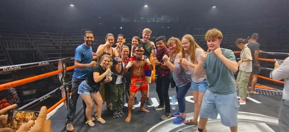 A group of people in a boxing ring, some holding drinks and posing for a photo. 1