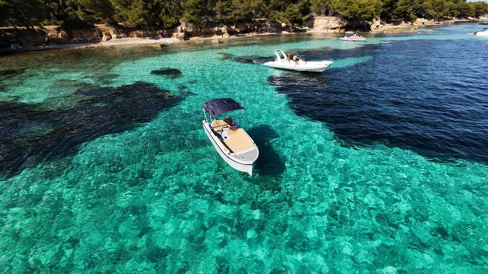 A clear turquoise sea with boats, rocky coastline, and dense green trees. 5