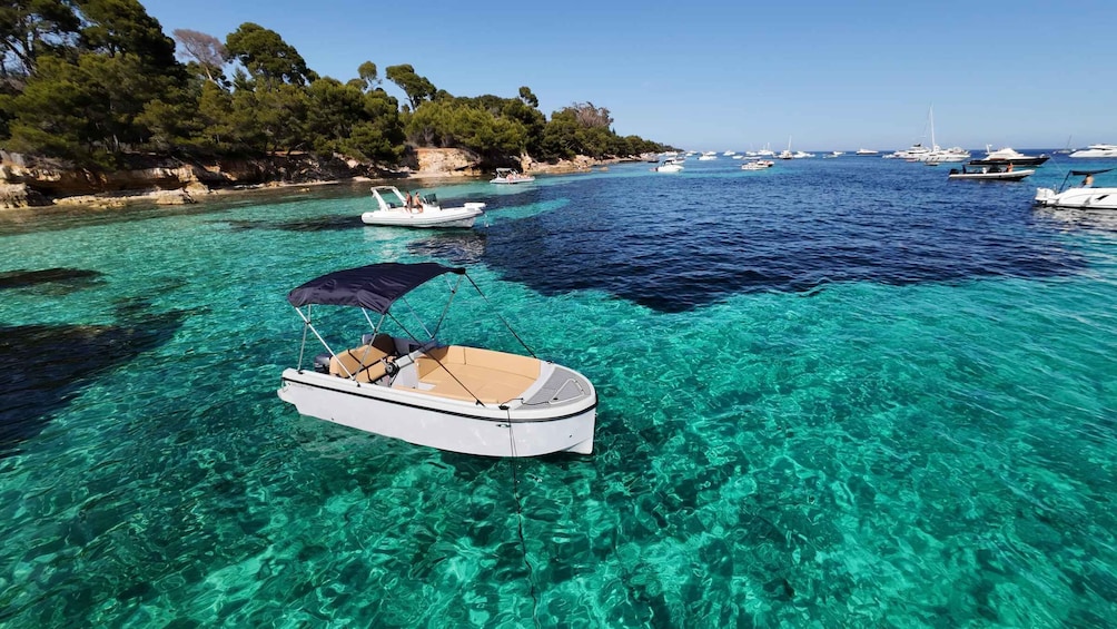 A clear turquoise sea with boats anchored near a rocky shoreline. 1