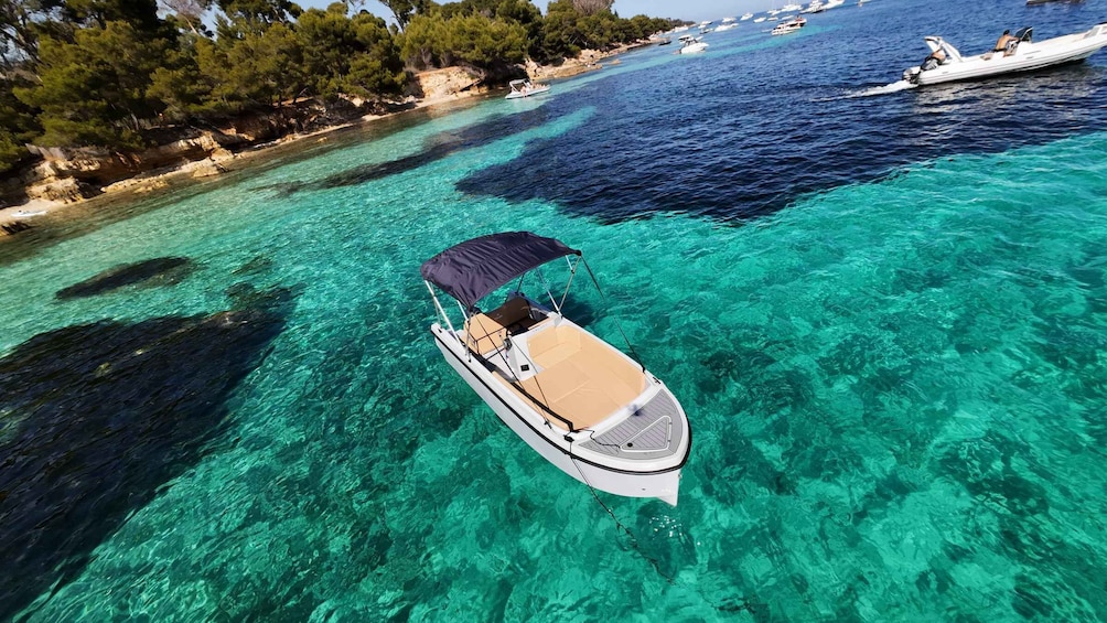 A clear turquoise sea with a boat anchored in the middle, surrounded by rocky shores and dense trees. 4