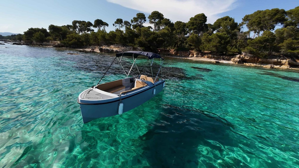 A boat anchored in clear turquoise waters with a rocky shoreline and dense trees in the background. 2