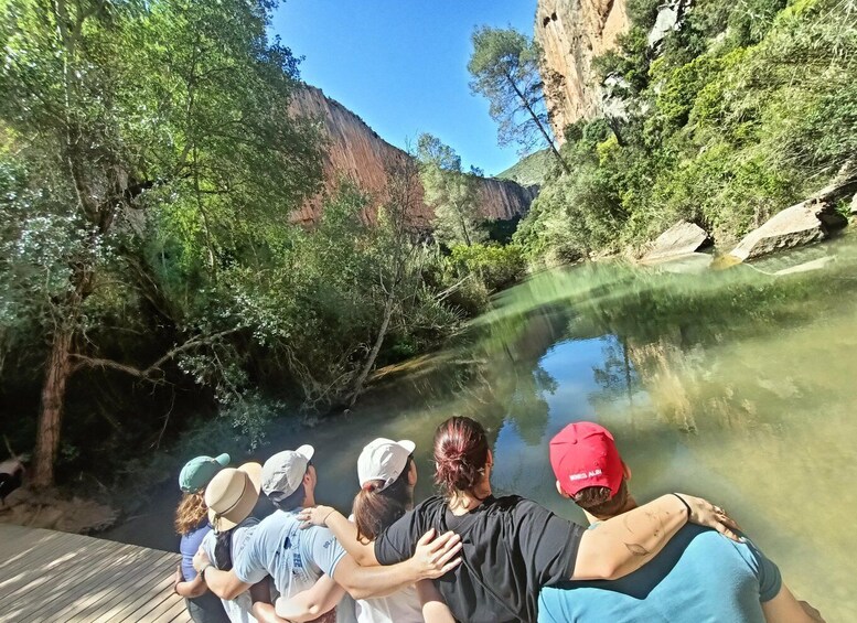A group of people standing on a wooden deck overlooking a river with clear water, surrounded by greenery and a rocky cliff. 2