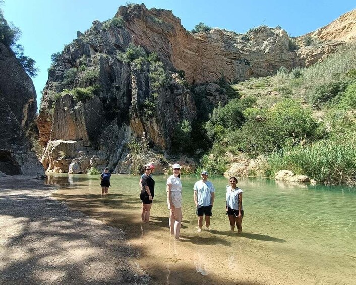 A group of people standing by a clear river in a canyon with rocky cliffs. 3
