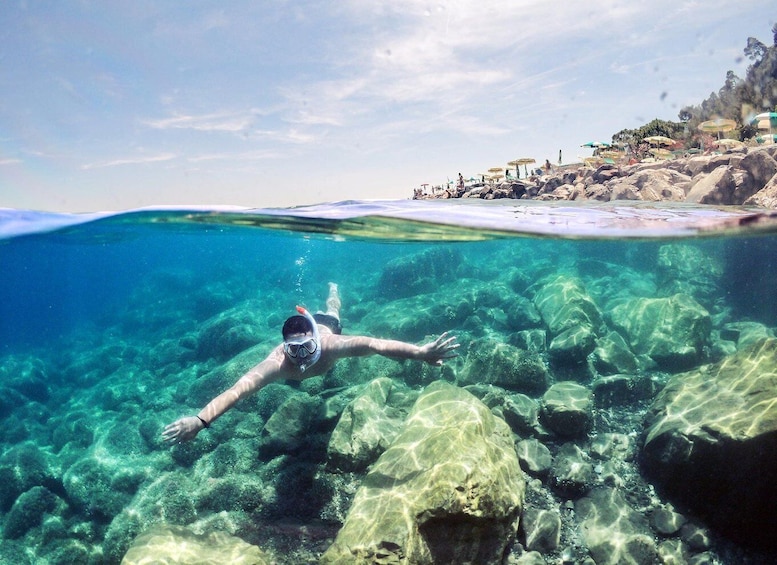 A person snorkeling underwater near a rocky shore with clear water. 5