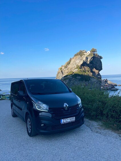 A black van parked on a gravel road with a rocky cliff and ocean in the background. 2