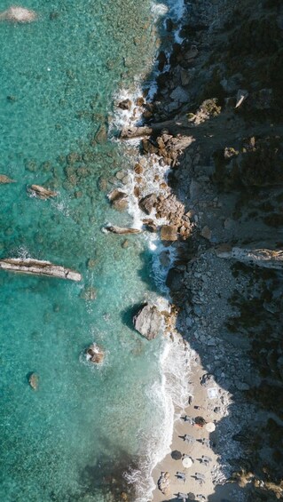 A rocky shoreline with clear turquoise water, scattered rocks, and a few sun loungers on the beach. 3