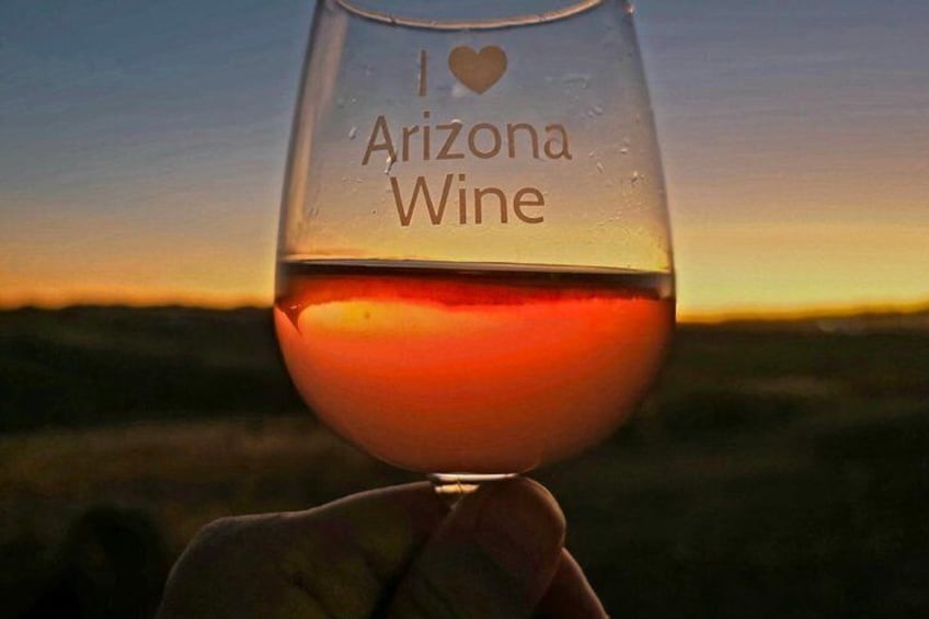 Ett vinglas med texten ”Jag älskar Arizona-vin” på, som hålls framför en solnedgång. 2