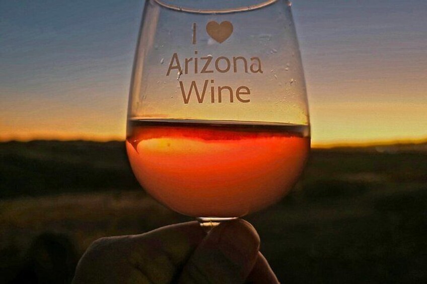 A glass of wine with 'I ♥ Arizona Wine' written on it, held against a sunset background. 2
