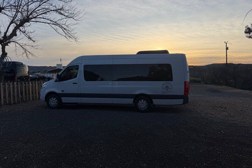 A white van parked on a gravel road with a sunset in the background. 4