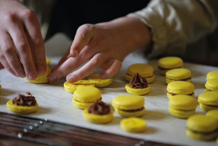 Hænder samler gule macarons med chokoladefyld. 5
