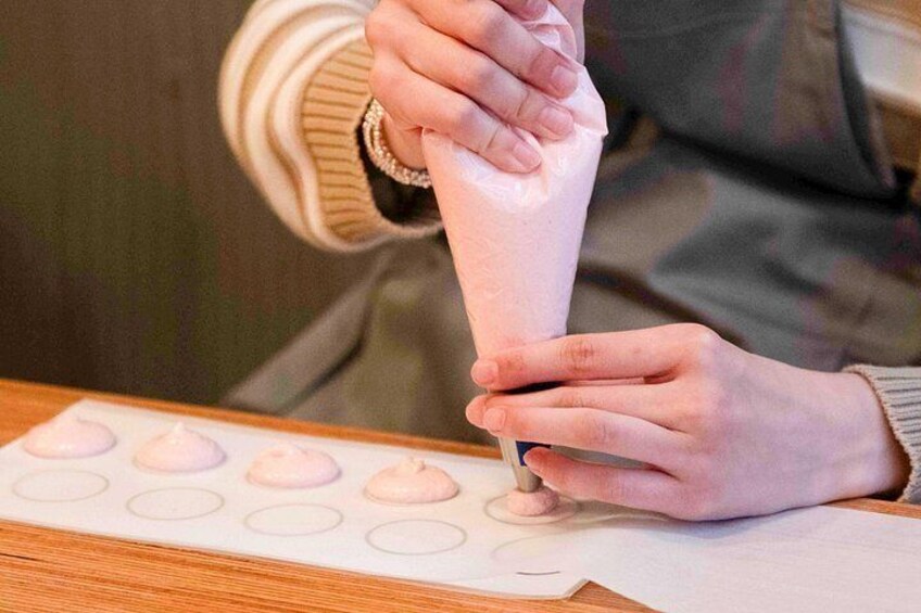 A person using a piping bag to fill cupcake liners with a pink substance. 3