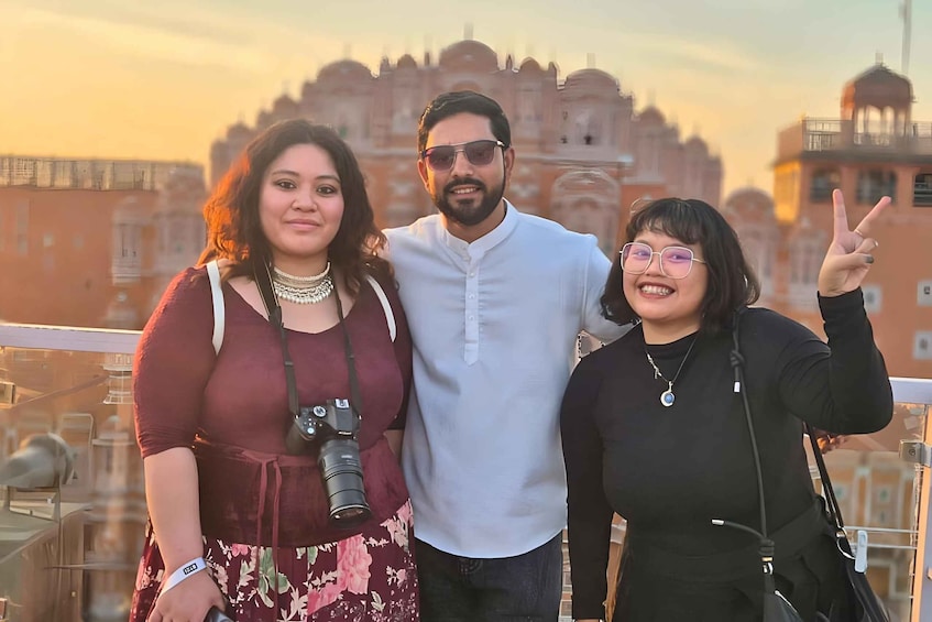 Three people standing on a balcony with a historic building in the background. 3