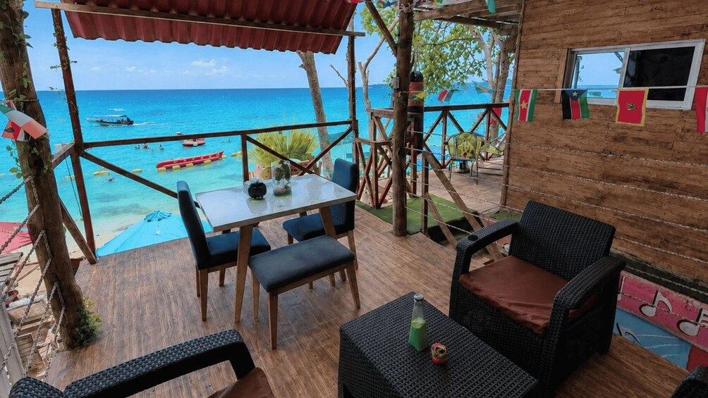 A wooden deck with a table and chairs overlooking a beach with boats. 3