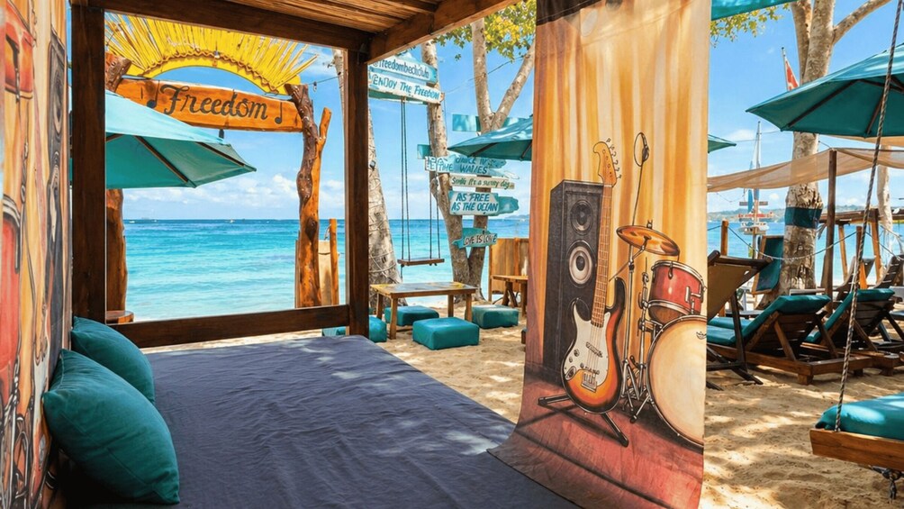 A beachside room with a view of the ocean, featuring a bed, musical instruments, and beach chairs. 2