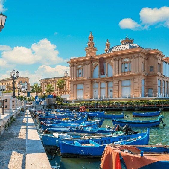 A canal with blue boats docked along the waterfront, a historic building with a dome and towers, and a clear blue sky. 3