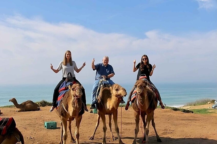 Three people riding camels on a beach with the sea in the background. 5
