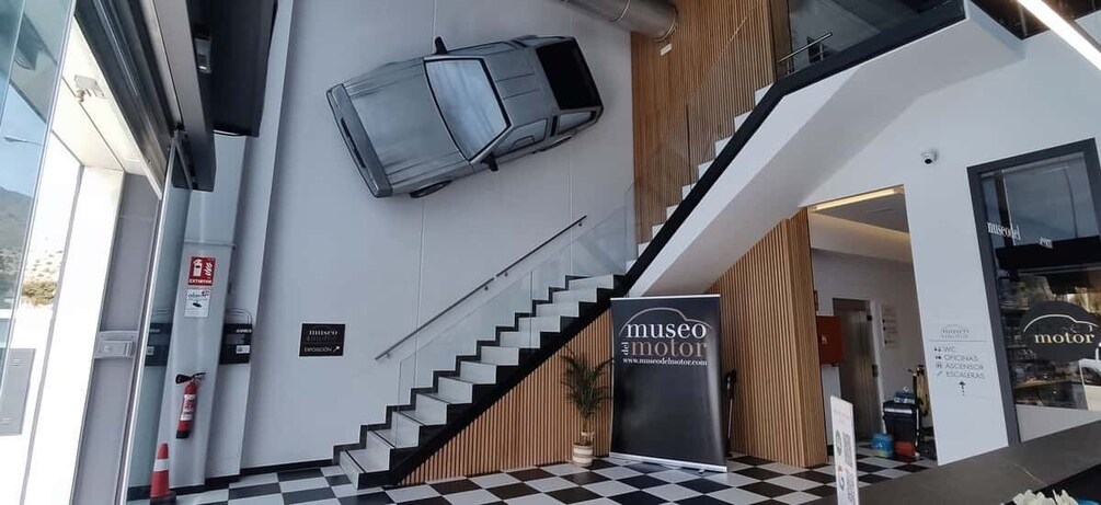 A modern building with a checkered floor, a staircase, and a car hanging from the ceiling. 1