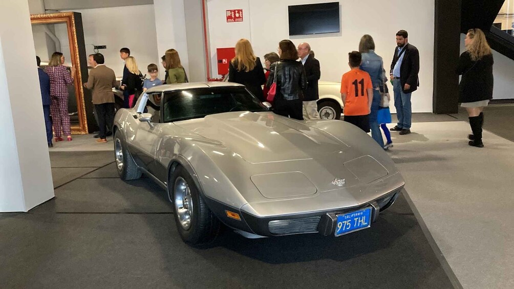 A silver sports car on display at an indoor event with people observing it. 4