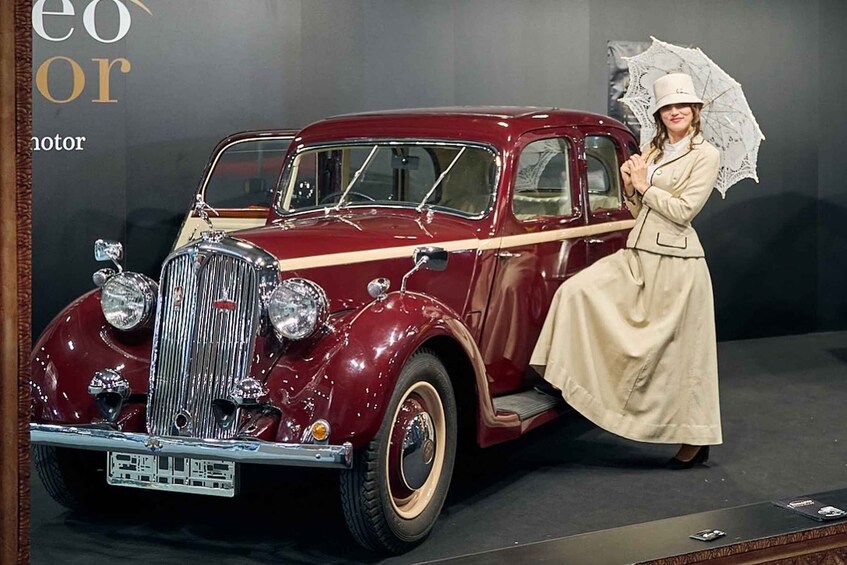 A vintage car with a woman standing beside it, holding an umbrella. 2