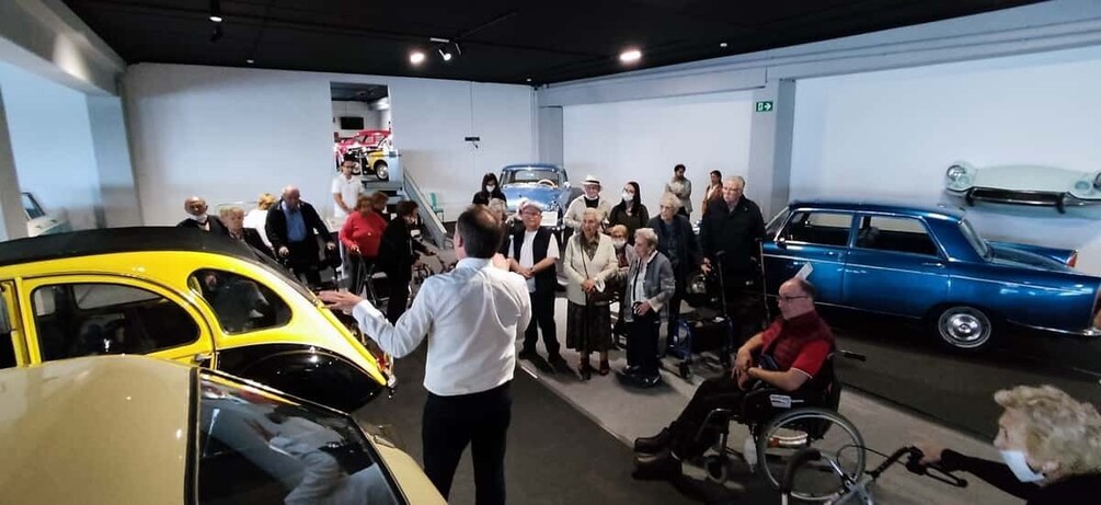 A group of people in a museum-like setting, observing vintage cars. 5
