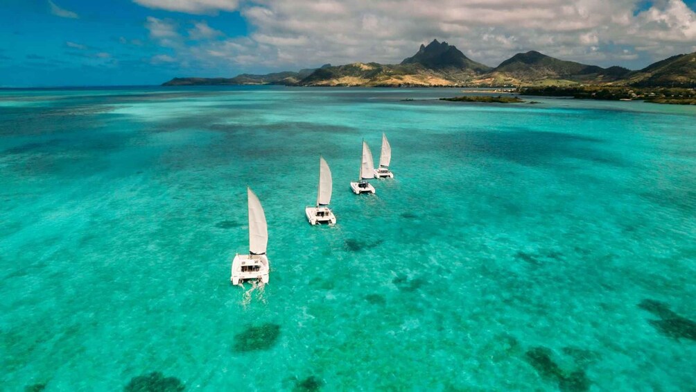 Drie zeilboten op turquoise water, met een bergachtig landschap op de achtergrond. 4