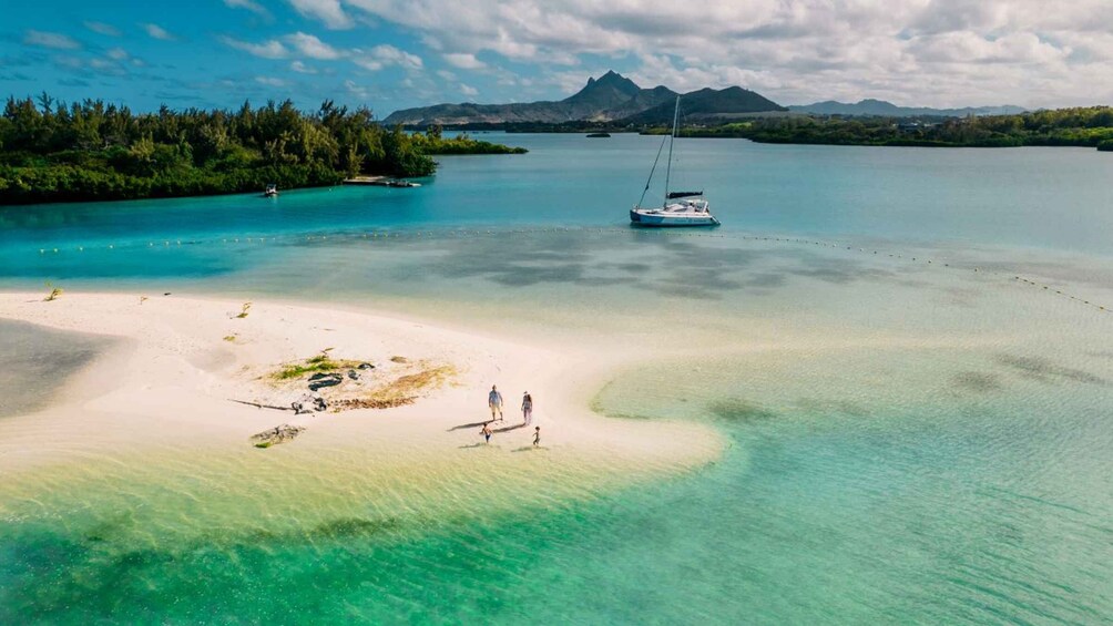 Een strand met helder turquoise water, een zeilboot en een bergachtig landschap op de achtergrond. 1