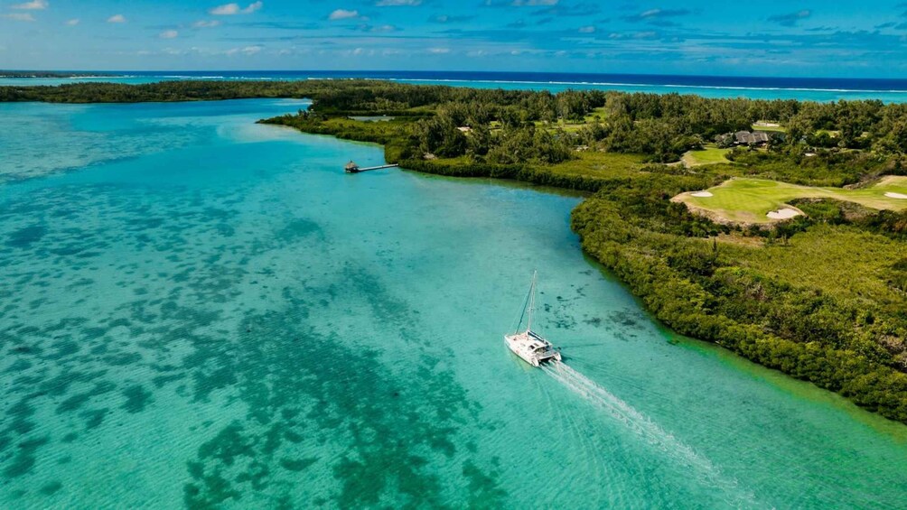 Een zeilboot op turquoise water, omgeven door weelderige begroeiing en een golfbaan. 5