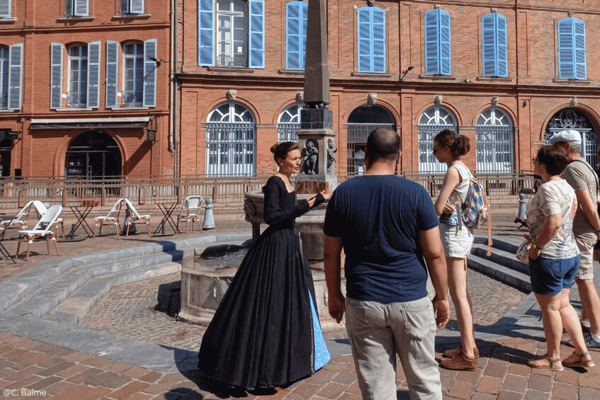 A historical building with red brick walls and blue shutters, a fountain, and people standing around. 5