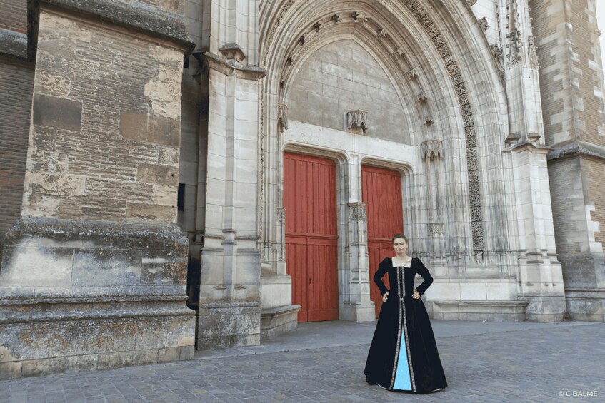 A person standing in front of a historic building with arched windows and red doors. 2