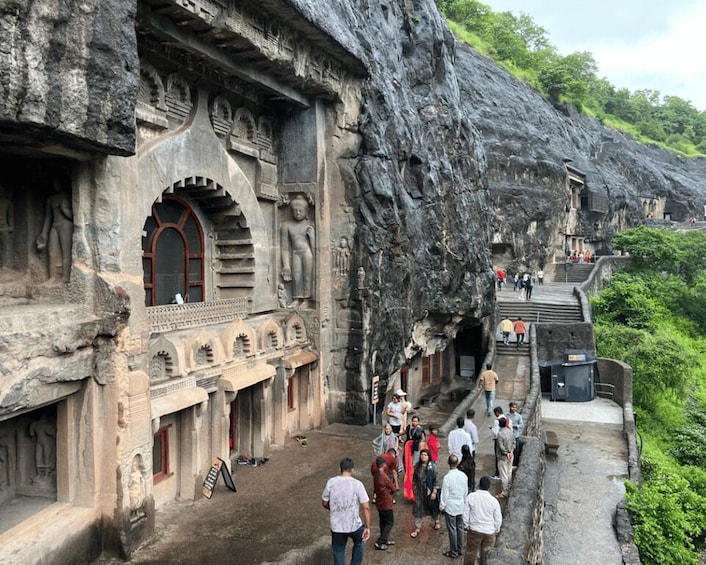 A historical rock-cut architecture with carved figures and a group of people walking in the foreground. 2