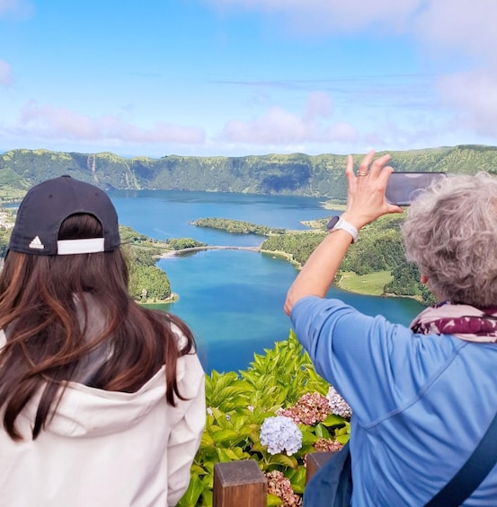 Two people overlooking a lake surrounded by greenery. 1