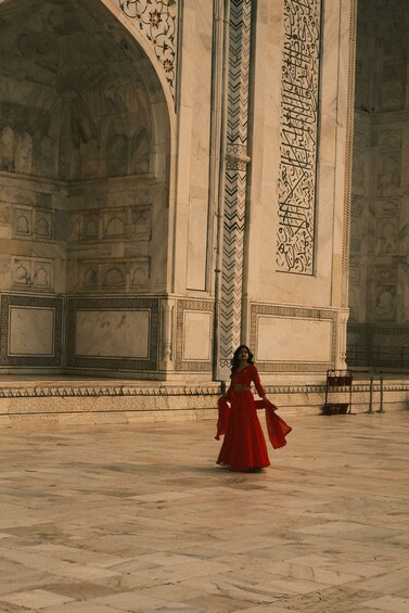 Une femme vêtue d’une robe rouge se promène devant un grand bâtiment orné, doté de motifs complexes et d’arcades. 1
