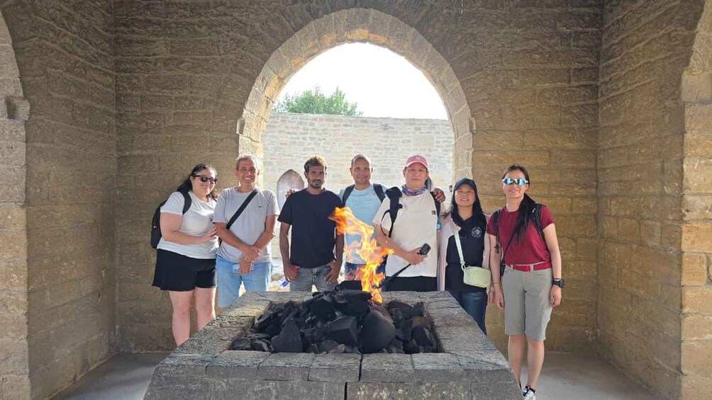A group of people standing in front of a stone structure with a fire burning in a pit. 5