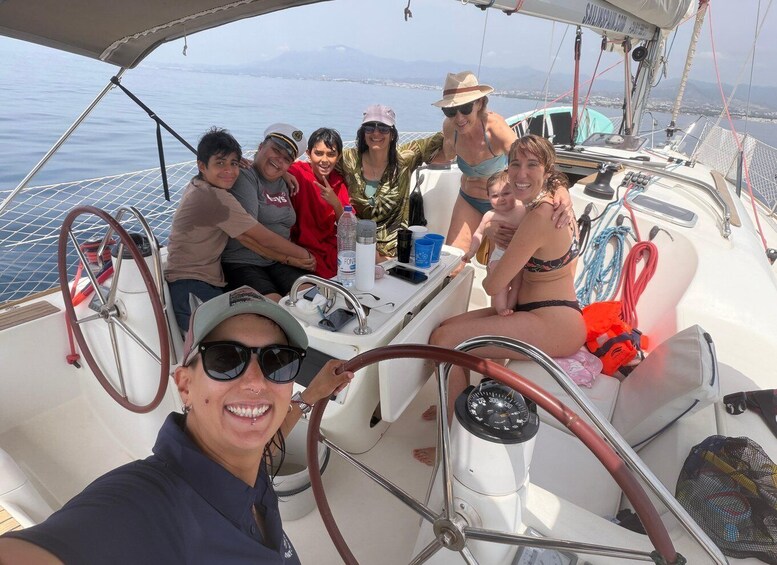 A group of people on a sailboat with a steering wheel, water bottles, and a person in a bikini. 2
