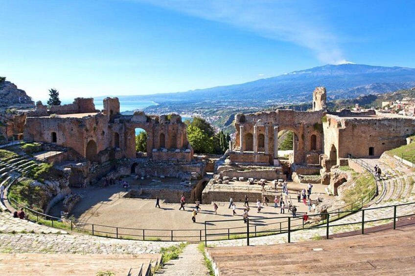 Ancient ruins with a large amphitheater, a stone pathway, and a mountainous backdrop. 1