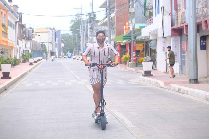 Une personne circule à trottinette électrique dans une rue bordée d’immeubles et de boutiques. 3