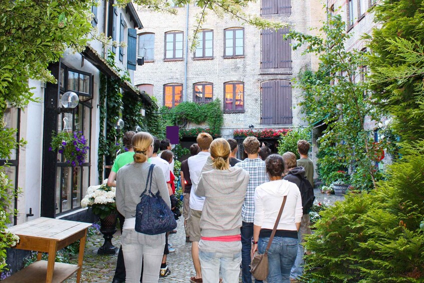 Un groupe de personnes se promène dans une ruelle étroite bordée d’immeubles et de verdure. 2