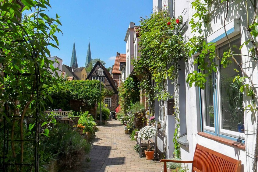 Un chemin pavé bordé d’une végétation luxuriante et de bâtiments traditionnels, avec, au loin, le clocher d’une église. 3