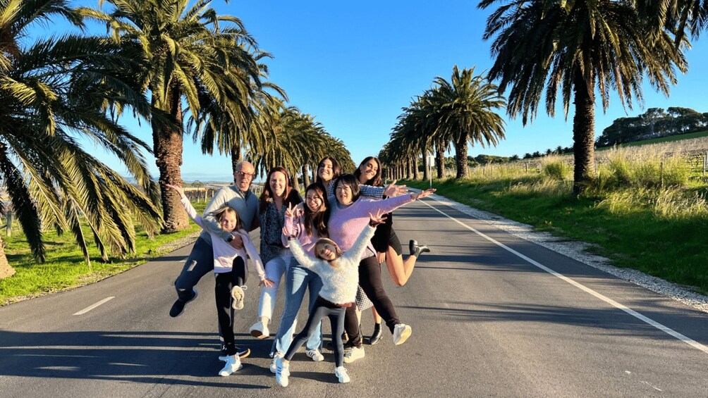 A group of people posing on a road with palm trees on both sides. 1