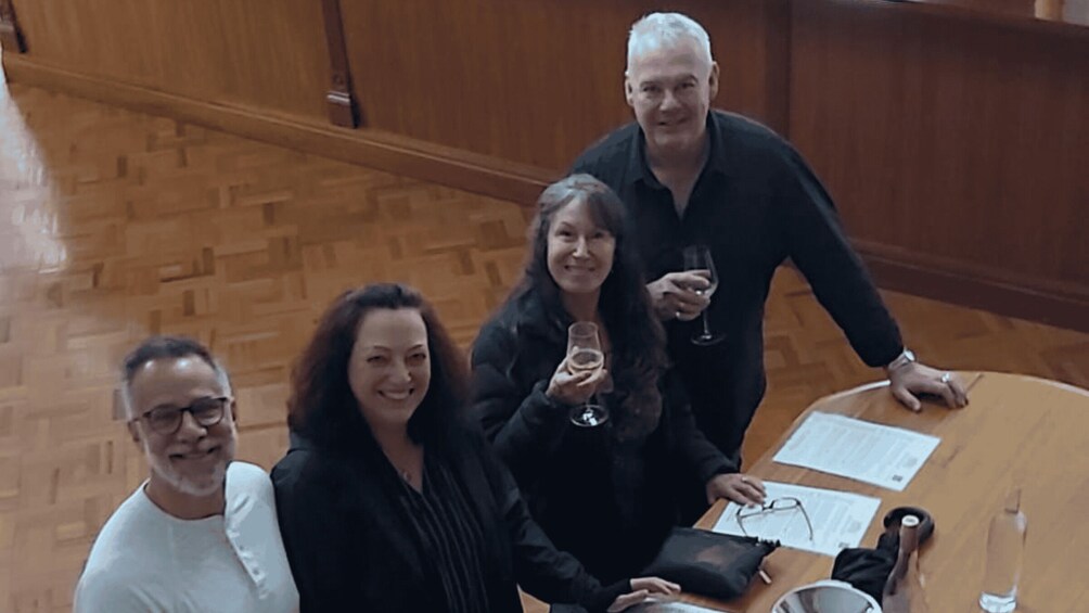 Four people standing around a table with papers and a glass. 4