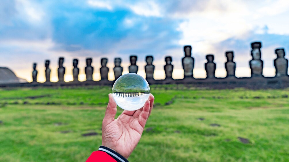 Une main tenant une boule de cristal dans laquelle on peut voir un paysage et, au fond, des statues Moaï. 2
