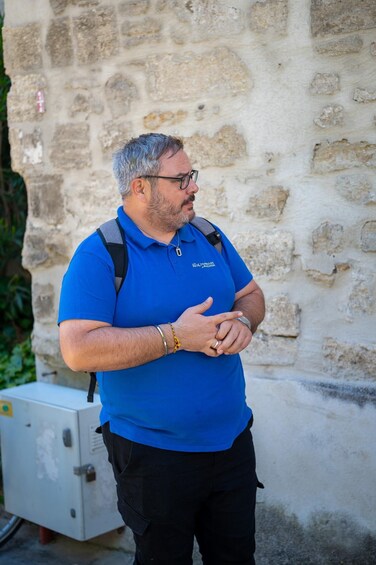 A man in a blue shirt with a backpack standing in front of a stone wall. 3