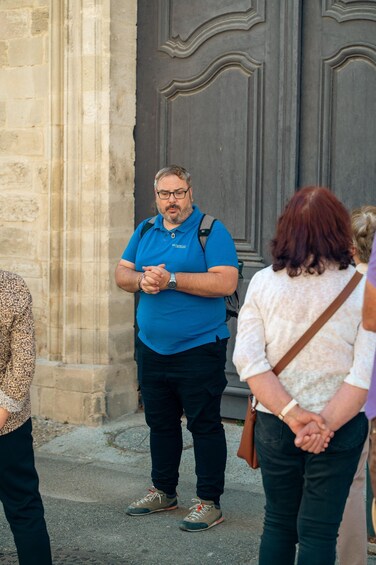 A man in a blue shirt standing in front of a stone building with a large door. 4