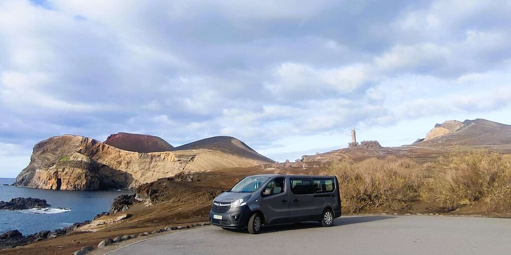 A gray van parked on a coastal road with cliffs and a lighthouse in the background. 1