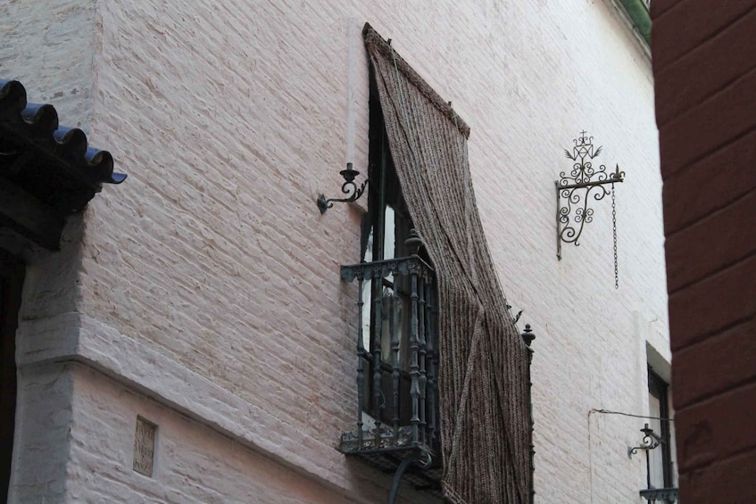 Un bâtiment avec une fenêtre entrouverte, une enseigne décorative en fer forgé et un mur en briques. 4