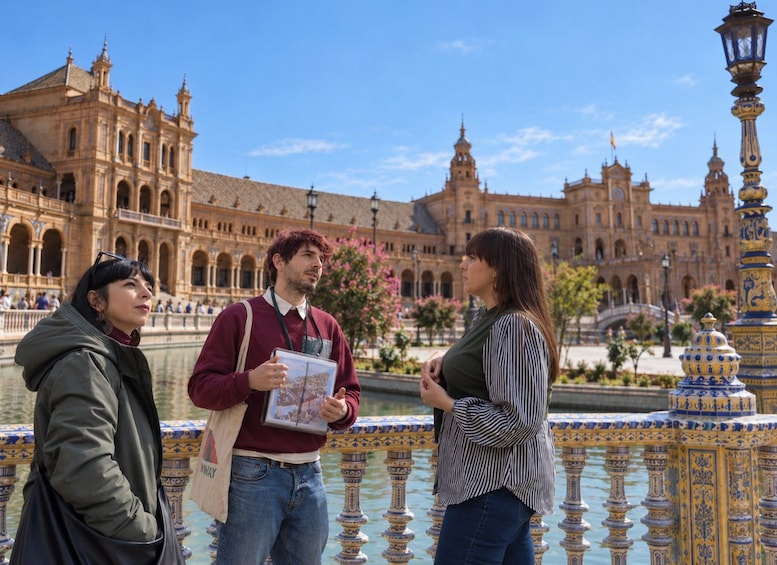 Trois personnes se tiennent près d’une balustrade décorative, avec un bâtiment historique en arrière-plan. 1
