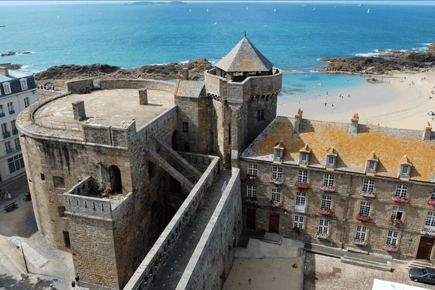 Una fortaleza de piedra histórica con una torre que domina una playa y el mar. 4