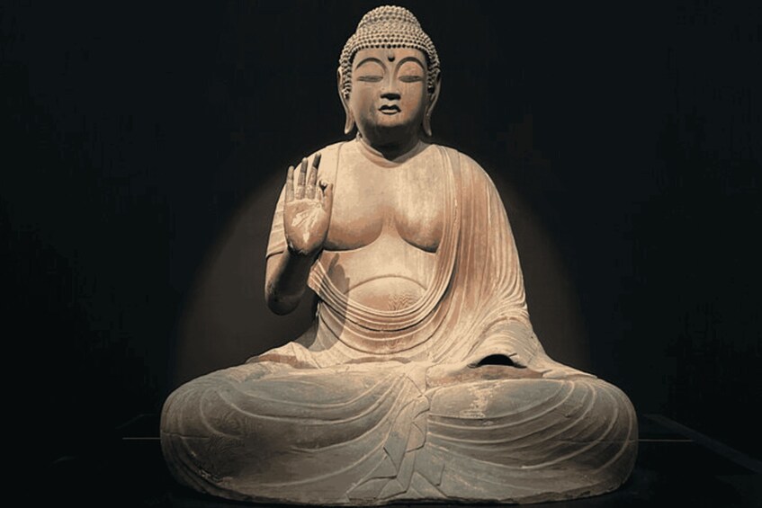 A seated Buddha statue with a raised hand, draped robes, and a serene expression. 3
