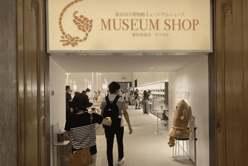 A museum shop with a sign in Japanese and English, people walking inside, and a display of a plush toy on a stand. 2