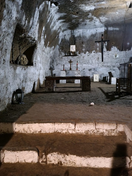 An interior of a cave with a wooden altar, a crucifix, and a religious icon. 5